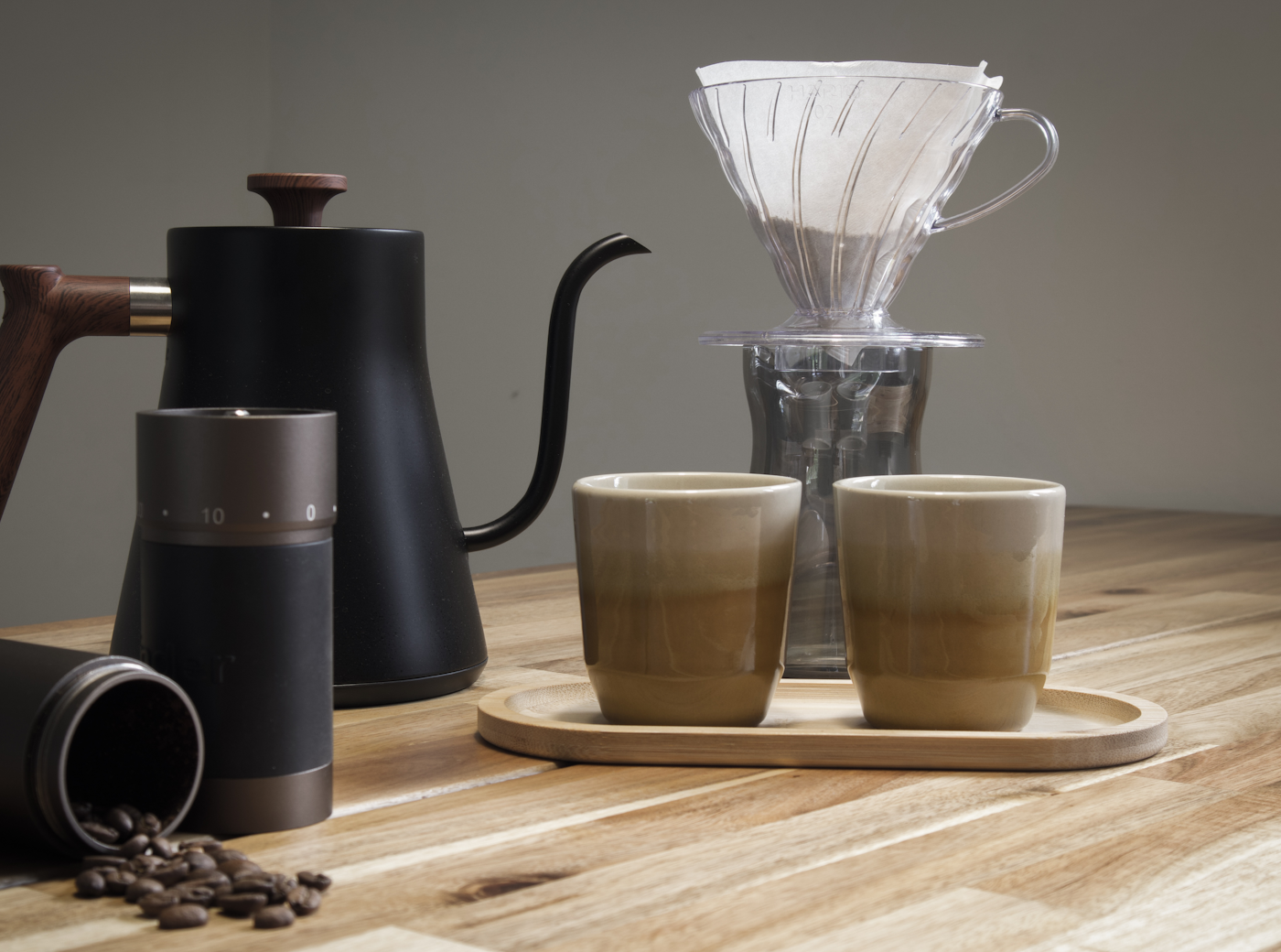 木のテーブルに置かれた手挽きコーヒーミルとコーヒー豆、ドリップケトル、ドリッパー、2つのカップ